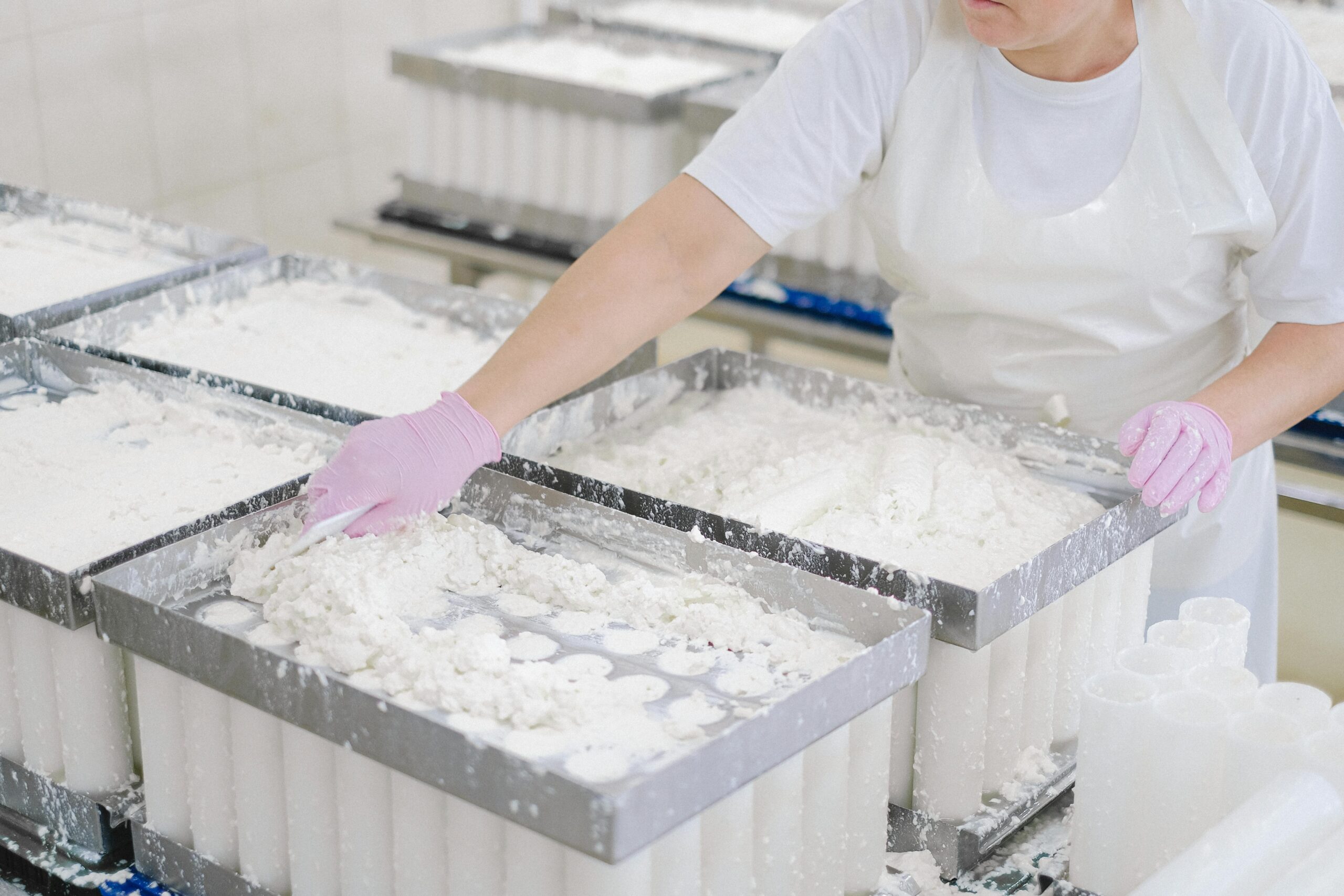 Worker in protective gear handling cheese curds in an industrial dairy setting.